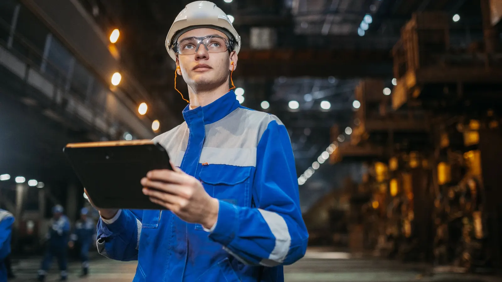 Ein Mitarbeiter mit Schutzhelm und Tablet in einer Werkshalle