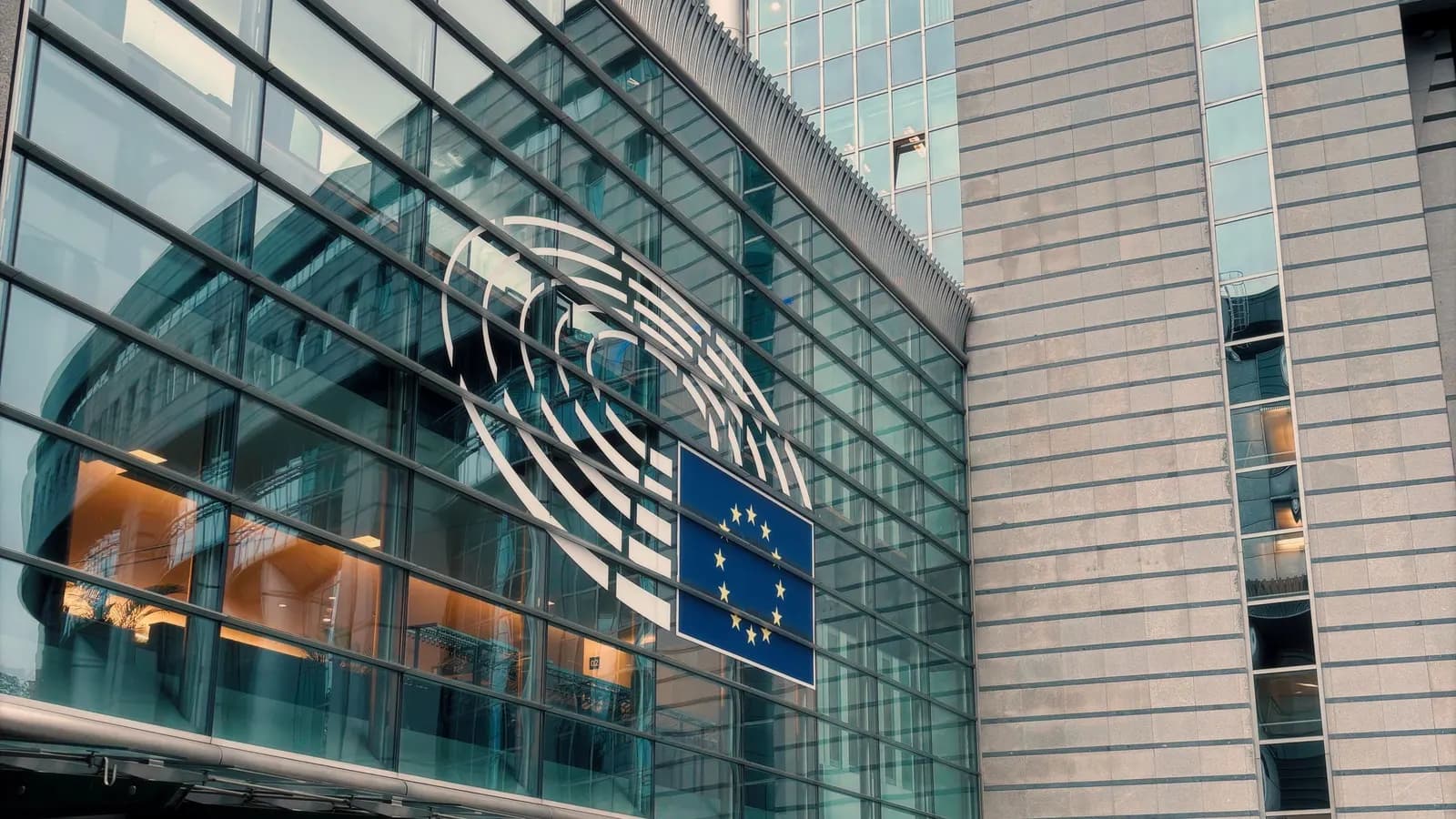 Glass facade of the European Parliament in Brussels with the Parliament logo and the European flag