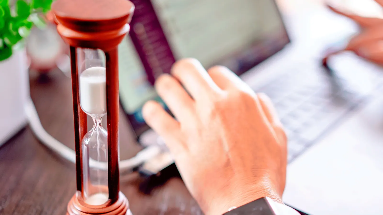 An hourglass next to a laptop on a desk — an image of the transition period being demanded for the PPWR